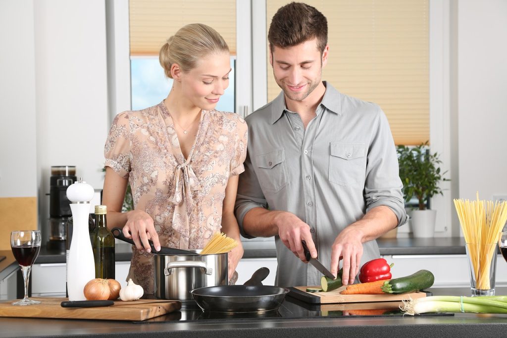Couple cooking together in modern kitchen, preparing fresh vegetables and pasta, enjoying a culinary experience