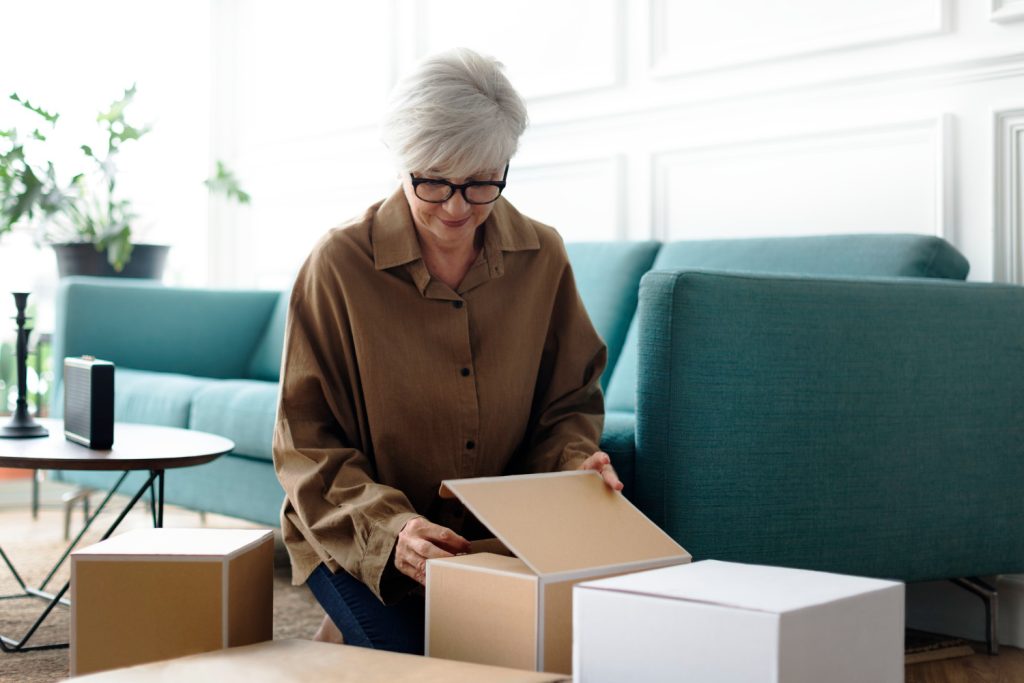 A woman relaxes on a couch, with several boxes around her, suggesting she is in the process of moving or unpacking