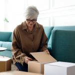 A woman relaxes on a couch, with several boxes around her, suggesting she is in the process of moving or unpacking